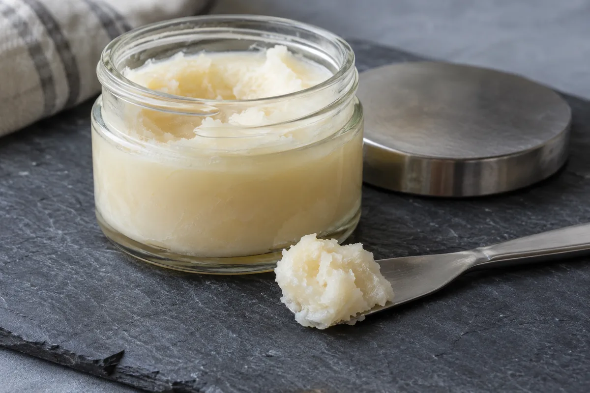 A jar of pale solid balm and a textured scoop on a metal spatula