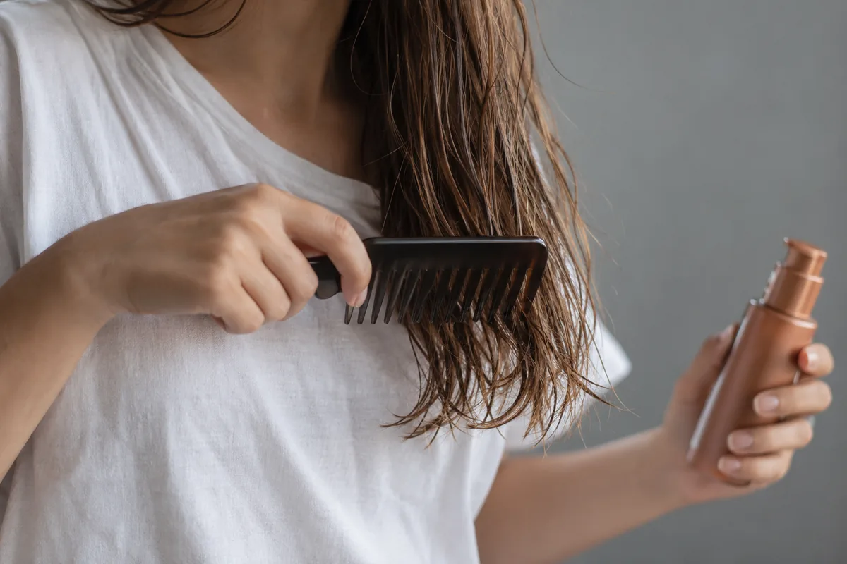 Damp hair ends over a white shirt with a wide-tooth comb and unlabelled treatment bottle