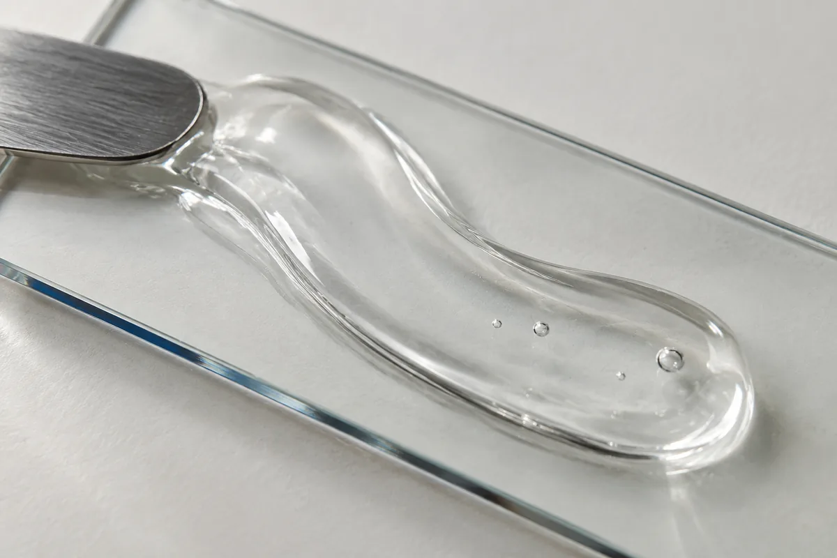 Clear cosmetic gel on a glass slide beside a metal spatula