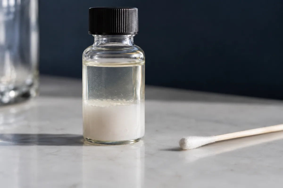 An unlabelled bottle with settled white sediment beside a cotton swab