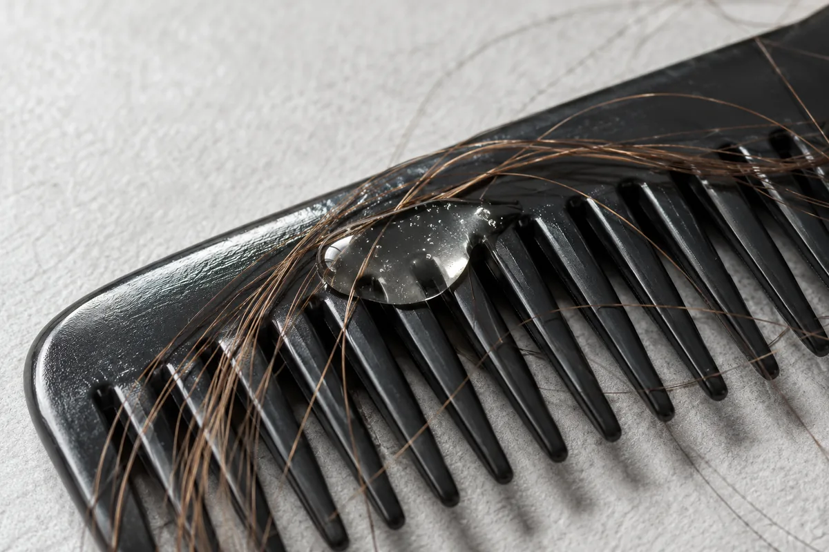 Transparent hair serum on a comb beside hair strands